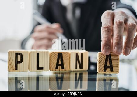 PIANO A, la parola è scritta su cubi di legno sullo sfondo di un uomo d'affari con un vestito nero a un tavolo. Foto Stock