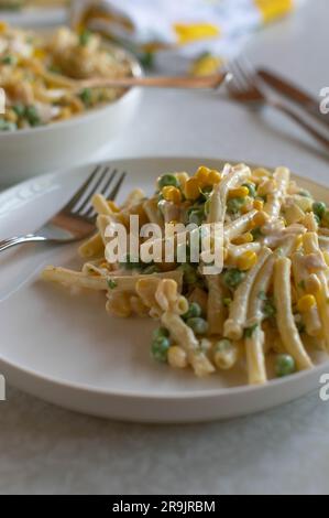 Piatto con insalata di pasta classica. Preparato con maionese, uova sode, piselli verdi, mais e salsiccia su un tavolo Foto Stock