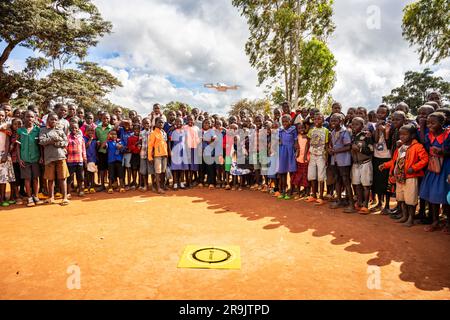 Gli scolari di una scuola malawia guardano mentre un UAV (drone) decolla dal loro terreno scolastico. Foto Stock