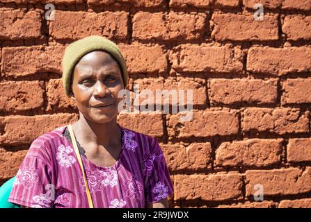 Ritratto di una donna malawiana seduta contro un muro di mattoni in un villaggio rurale Foto Stock