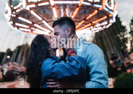 Coppia giovane che si baciano in un parco divertimenti la sera Foto Stock