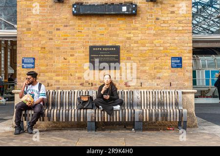 Un uomo e una donna siedono in una panchina sotto una targa per Hope Square fuori dalla stazione di Liverpool Street a Londra, Regno Unito Foto Stock