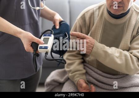 Giovane infermiera sorridente che prende la pressione sanguigna del vecchio Foto Stock