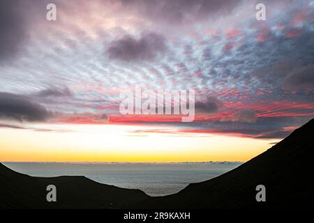 Nuvole panoramiche nel cielo all'alba su sagome di scogliere che circondano Gjogv, l'isola Eysturoy e le isole Faroe Foto Stock