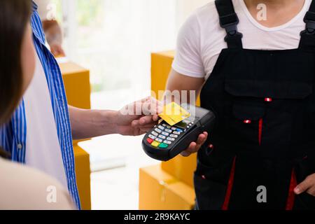 Giovane uomo e donna che paga le scatole di consegna con carta di credito, uomo e donna che accetta e tiene in mano le scatole dei pacchi di consegna dal corriere a casa Foto Stock