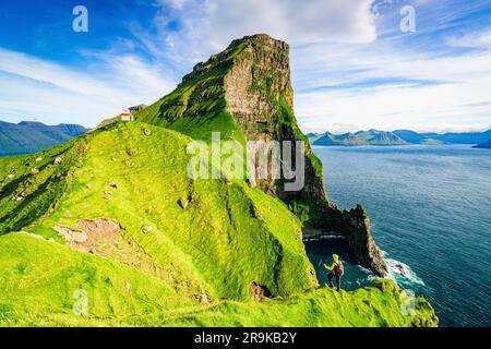 Vista ad alto angolo dell'uomo sulle scogliere, ammirando il faro di Kallur che si affaccia sull'oceano, sull'isola di Kalsoy, sulle isole Faroe, Danimarca Foto Stock