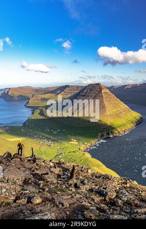 Uomo con bastoni da trekking che gode della vista di Vidareidi e della montagna Malinsfjall dalla cima delle rocce, dell'isola Vidoy e delle isole Faroe Foto Stock