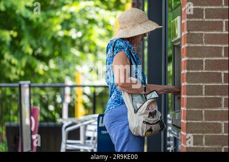 Signora anziana che ottiene soldi in contanti, presso un bancomat, un bancomat o un bancomat 'buca nel muro', nel Regno Unito. Foto Stock