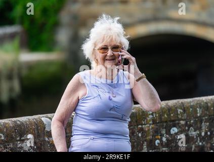 Signora anziana in piedi all'esterno che usa un telefono cellulare, un cellulare o uno smartphone per parlare con qualcuno. Donna anziana aggiornata con la tecnologia moderna, Regno Unito. Foto Stock