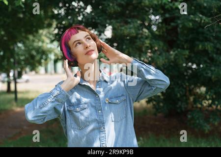 La donna con i capelli rosa e le cuffie ascolta la musica nel parco Foto Stock