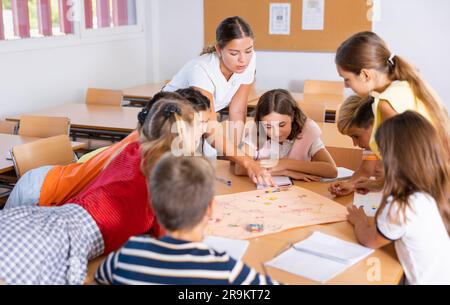 Schoolkids con insegnante che gioca a un tavolo educativo in classe Foto Stock