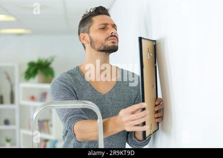 Repairman mettendo cornice immagine sulla parete Foto Stock