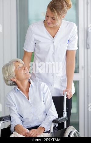 accompagnatore che spinge una donna anziana in sedia a rotelle Foto Stock