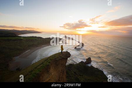 Viaggiatore in giacca gialla godendosi la vista panoramica sul mare del faro di Castle Point sulla ripida collina che torreggia sul Mare di Tasman e sull'Oceano Pacifico Foto Stock