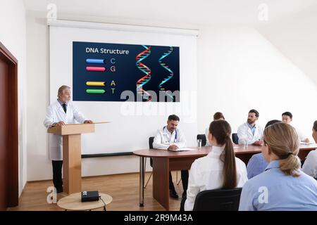 Lezione di biochimica. Altoparlante senior vicino allo schermo di proiezione con illustrazione. Professori e pubblico nella sala conferenze Foto Stock