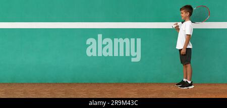 Un bambino carino vicino al muro verde sul campo da tennis. Design banner con spazio per il testo Foto Stock