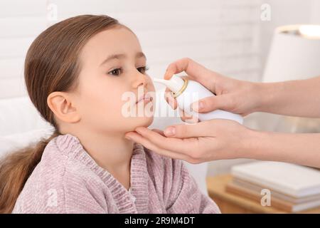 Madre che usa spray nasale per trattare la sua bambina al chiuso, primo piano Foto Stock