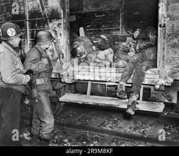 Due soldati americani che guardano prigionieri morti su un treno ferroviario in un campo di concentramento non identificato, Germania, Stati Uniti Army Signal Corps, aprile 1945 Foto Stock