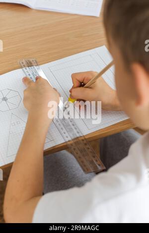 Un ragazzo carino crea un disegno con un righello e una matita. Lezioni a casa. Geometria e disegno. Foto Stock
