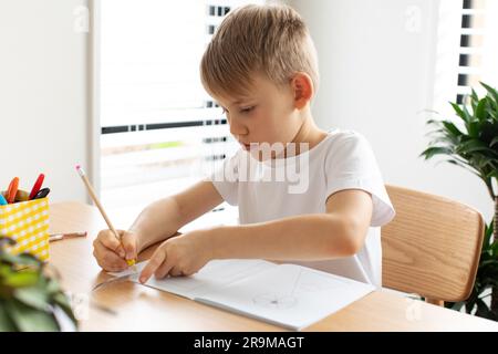 Un ragazzo carino crea un disegno con un righello e una matita. Lezioni a casa. Geometria e disegno. Foto Stock