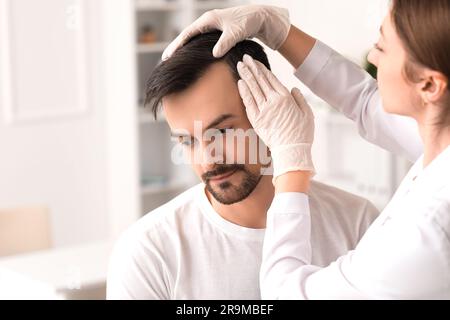 Medico che esamina i capelli di un giovane in clinica, primo piano Foto Stock