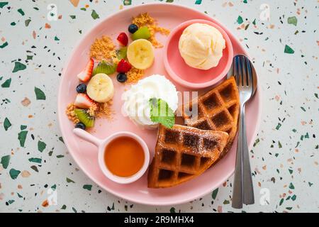 Waffle con gelato, panna montata, banana, fragole, kiwi e miele. Foto Stock