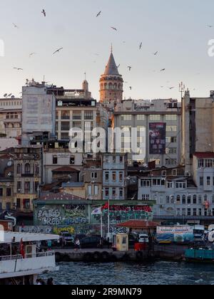 Il lungomare di Kadakoy sul fiume Corno d'Oro in una sera d'estate, mentre i gabbiani volano in alto e le persone visitano la città dalla Torre di Galata. Istanbul, Turchia. Foto Stock