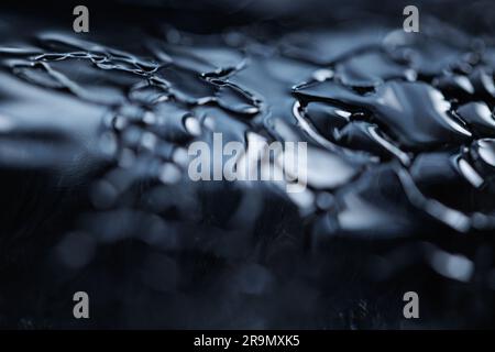 Un macro shot di gocce d'acqua su una superficie nera per lo sfondo degli sfondi Foto Stock