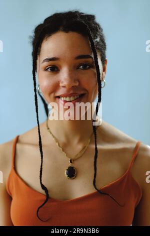 Giovane donna adulta sorridente con trecce. Indossa una canotta arancione nelle riprese in studio Foto Stock