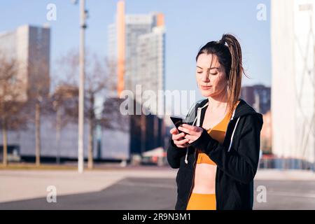 donna sportiva di bellezza che usa un cellulare in città Foto Stock