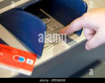 ILLUSTRAZIONE - 23 giugno 2023, Renania settentrionale-Vestfalia, Königswinter: Un cliente bancario utilizza la sua carta giro, che presenta il logo girocard (r) e il logo Maestro rosso e blu (2-r), per prelevare contanti da un bancomat. La funzione Maestro delle carte giro, che consente pagamenti e prelievi di contanti all'estero, non sarà più disponibile sulle nuove carte in futuro. Dal 1° luglio 2023, non verranno emesse nuove carte Maestro. Foto: Thomas Banneyer/dpa Foto Stock