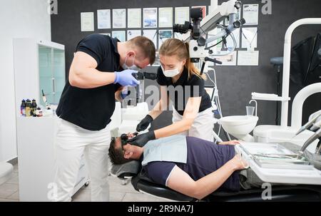 Vista laterale dei dentisti che fissano i denti e scattano foto del risultato. Medici che indossano uniformi bianche e nere, maschere e guanti, lavorano in clinica odontoiatrica. Concetto di assistenza sanitaria, odontoiatria. Foto Stock