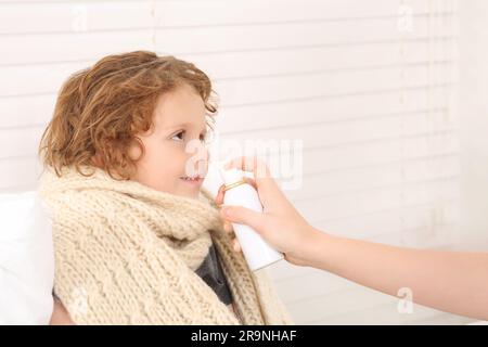 Madre che usa spray nasale per trattare il suo piccolo figlio al chiuso, primo piano Foto Stock