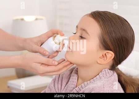 Madre che usa spray nasale per trattare la sua bambina al chiuso, primo piano Foto Stock