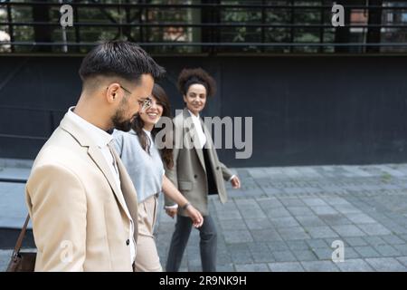 Un gruppo di colleghi che camminano all'esterno di fronte agli edifici di uffici discutono del piano aziendale. Imprenditori esperti di marketing e vendita che parlano di idee e m Foto Stock