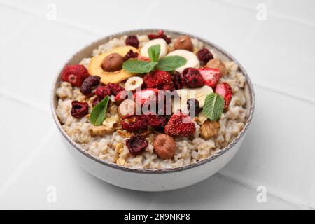 Farina d'avena con frutta liofilizzata, noci e menta su un tavolo piastrellato bianco, primo piano Foto Stock
