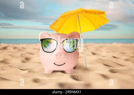 Sconti per le vacanze. Salvadanaio vicino all'ombrellone sulla spiaggia sabbiosa vicino al mare. Riflesso delle foglie di palmo negli occhiali da sole Foto Stock