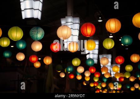 Molte lanterne di carta cinesi rotonde appese al buio. Molte decorazioni colorate e festose preparate per festeggiare le vacanze in stile orientale Foto Stock