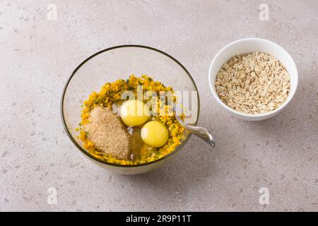 Recipiente di vetro con zucca tritata, zucchero di canna, uova e una ciotola di avena su sfondo beige. Cucinare deliziosi e sani pastri autunnali fatti in casa Foto Stock