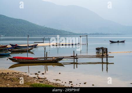 Una foto che si affaccia su piccole barche ancorate in una laguna vietnamita con montagne sullo sfondo. Foto Stock