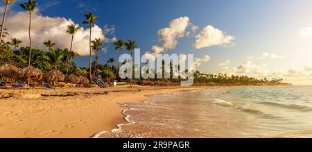 Palme da cocco sulla spiaggia di sabbia bianca contro il colorato tramonto a Punta Cana, Repubblica Dominicana. Sagome scure di palme e nuvolose Foto Stock