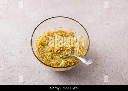 Recipiente di vetro con zucca tritata mista, uova, zucchero e farinata d'avena su sfondo beige. Cucinare deliziosi pasticcini autunnali fatti in casa. Foto Stock