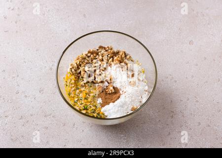 Recipiente in vetro con zucca tritata mista, uova, zucchero, farina d'avena e farina, noci e cannella su uno sfondo ruvido beige. Cucinare deliziosi piatti fatti in casa Foto Stock