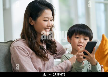 giovane madre asiatica seduta sul divano di famiglia mantenendo la compagnia con il figlio di cinque anni Foto Stock