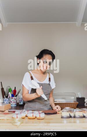 La pasticceria donna con un sacchetto di pasticcini in mano spreme la panna su una torta in una pasticceria. Foto Stock