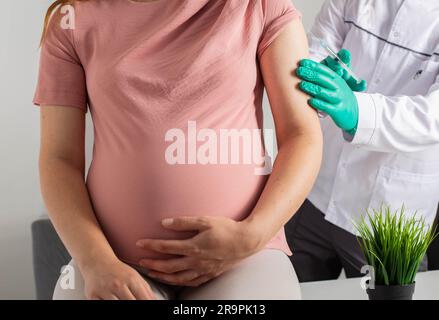 Un medico in guanti medici vaccina una ragazza incinta contro influenza, covid e pertosse. Infezione Foto Stock