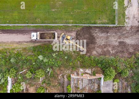 Vista aerea di un escavatore in funzione per rimuovere la terra e caricarla in un dumper su un cantiere edile. Foto Stock