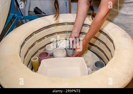 Primo piano di mani che mettono l'argilla cruda nel forno, forno per arrostire prodotti fatti a mano in argilla non cotta, ceramiche non finite e utensili. Forno in ceramica moderno Foto Stock