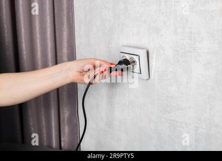 La ragazza rimuove erroneamente la spina elettrica dalla presa e la rompe. Pericolo di scossa elettrica. Spazio di copia per il testo Foto Stock