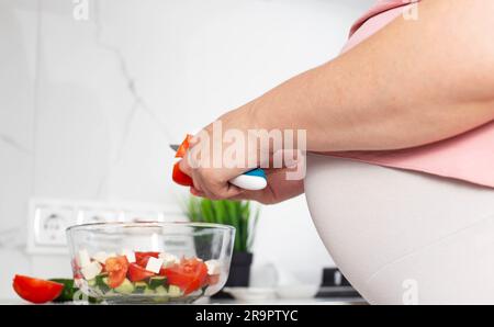 Una ragazza incinta prepara un'insalata di verdure di cetrioli e pomodori. Il concetto di nutrizione delle donne incinte con vitamine e macronutrienti in v Foto Stock